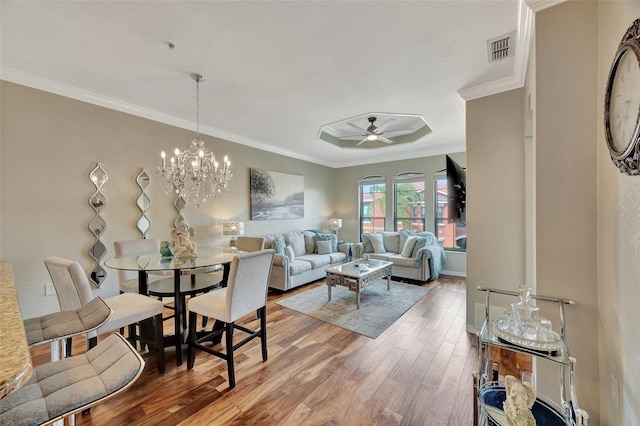 living room with ceiling fan with notable chandelier, wood-type flooring, and ornamental molding