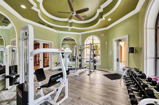 gym with french doors, ornamental molding, a tray ceiling, ceiling fan, and hardwood / wood-style floors