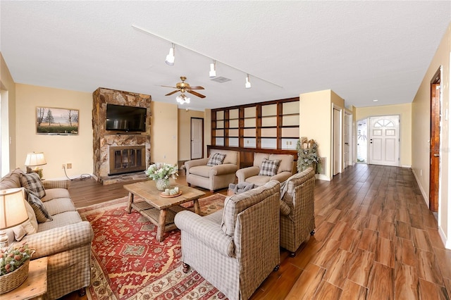 living room with ceiling fan, a stone fireplace, a textured ceiling, and hardwood / wood-style flooring