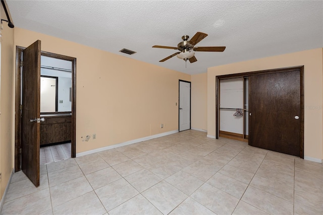 unfurnished bedroom featuring ceiling fan, light tile patterned floors, a textured ceiling, and ensuite bath