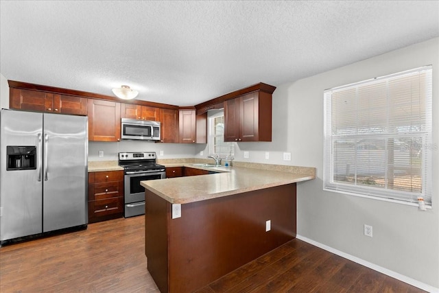 kitchen featuring sink, dark wood-type flooring, stainless steel appliances, a textured ceiling, and kitchen peninsula