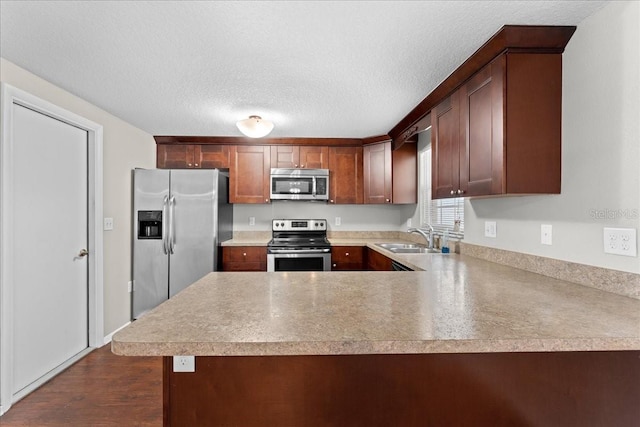 kitchen featuring sink, dark wood-type flooring, stainless steel appliances, a textured ceiling, and kitchen peninsula