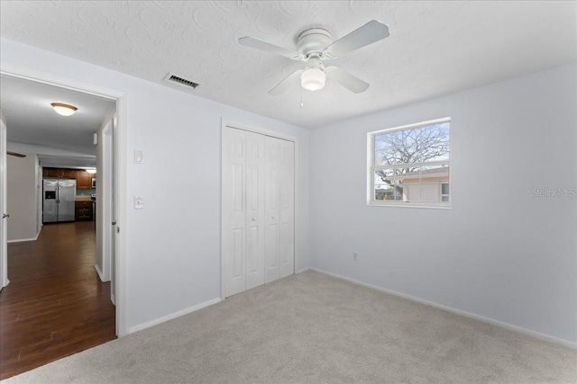 unfurnished bedroom with stainless steel refrigerator with ice dispenser, a textured ceiling, a closet, ceiling fan, and carpet