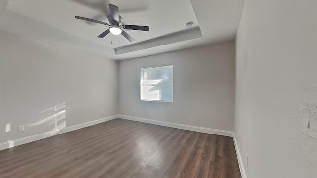 unfurnished room with a raised ceiling, ceiling fan, and dark hardwood / wood-style flooring