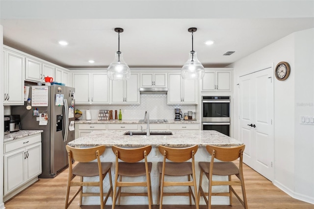 kitchen with sink, white cabinetry, hanging light fixtures, appliances with stainless steel finishes, and an island with sink