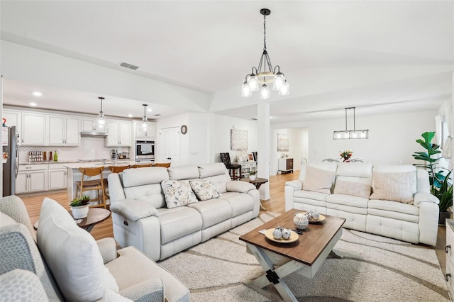 living room featuring lofted ceiling, a chandelier, and light hardwood / wood-style floors