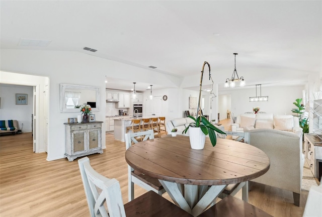 dining space with a chandelier, vaulted ceiling, and light wood-type flooring