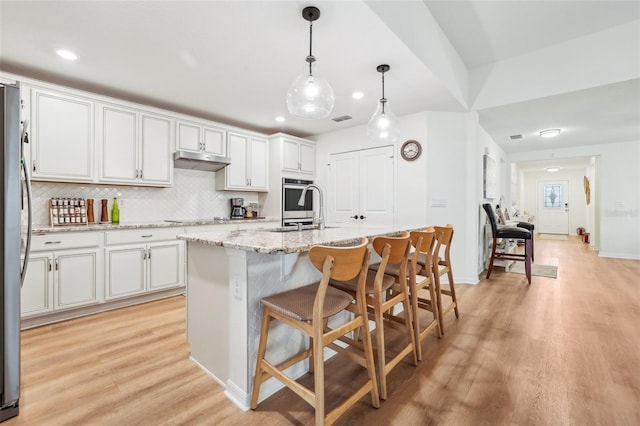 kitchen with appliances with stainless steel finishes, decorative light fixtures, an island with sink, white cabinets, and light stone counters