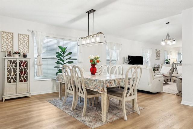 dining area with an inviting chandelier, vaulted ceiling, and light wood-type flooring