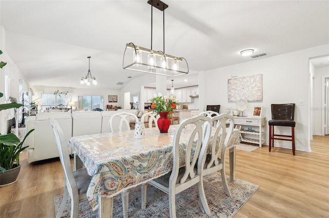 dining space with lofted ceiling, light hardwood / wood-style flooring, and a notable chandelier