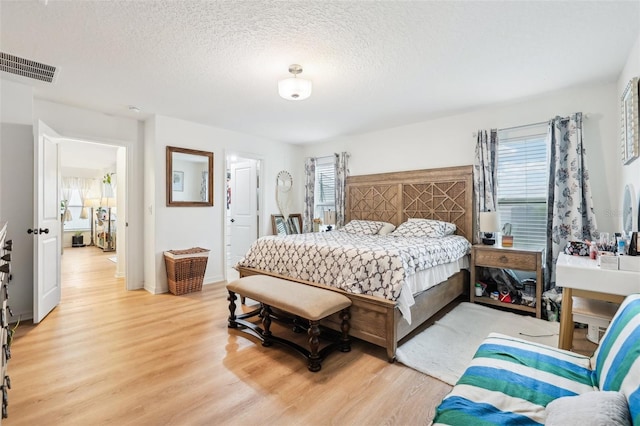 bedroom featuring a textured ceiling, light hardwood / wood-style floors, and ensuite bath