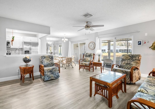 living room featuring sink, a textured ceiling, light hardwood / wood-style floors, and a healthy amount of sunlight