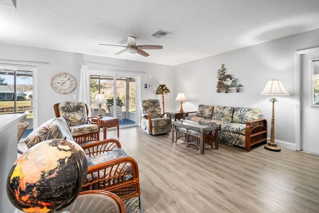 living room featuring ceiling fan, plenty of natural light, light hardwood / wood-style floors, and a textured ceiling