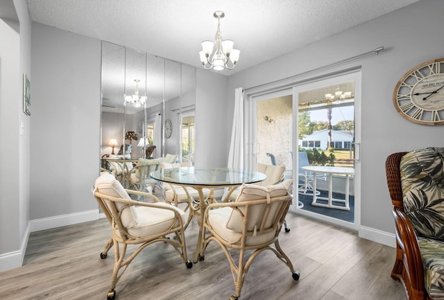 dining area with light hardwood / wood-style floors, a textured ceiling, and a notable chandelier