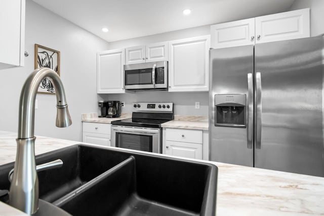 kitchen with white cabinetry, appliances with stainless steel finishes, sink, and light stone counters