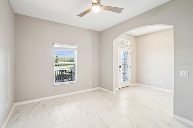 spare room with arched walkways, marble finish floor, ceiling fan, and baseboards