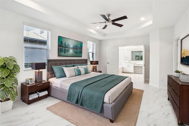 bedroom with a tray ceiling, marble finish floor, recessed lighting, a ceiling fan, and ensuite bath