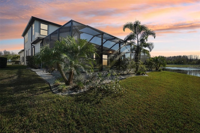 exterior space with stucco siding, glass enclosure, a lawn, and a water view