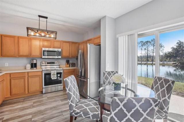 kitchen with decorative light fixtures, light wood-type flooring, a water view, and appliances with stainless steel finishes