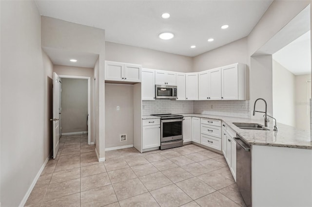 kitchen with sink, appliances with stainless steel finishes, light stone counters, white cabinets, and kitchen peninsula