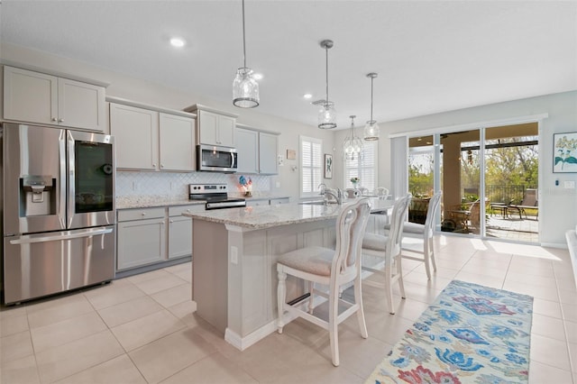 kitchen with gray cabinetry, decorative light fixtures, stainless steel appliances, and a center island with sink