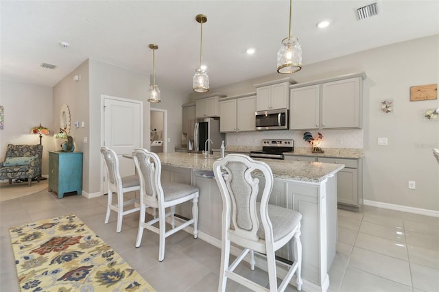 kitchen with gray cabinets, decorative light fixtures, decorative backsplash, stainless steel appliances, and a center island with sink