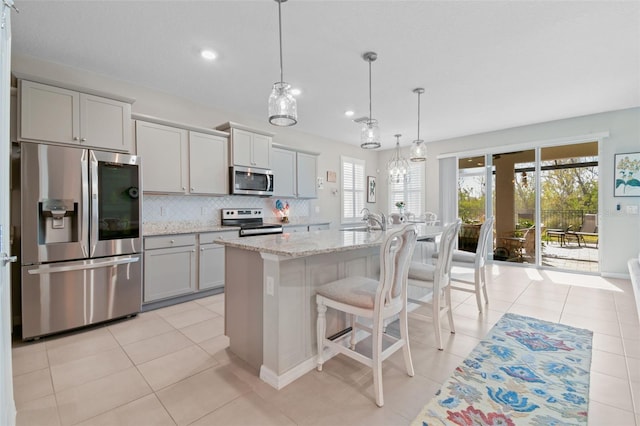 kitchen featuring pendant lighting, gray cabinets, appliances with stainless steel finishes, backsplash, and an island with sink