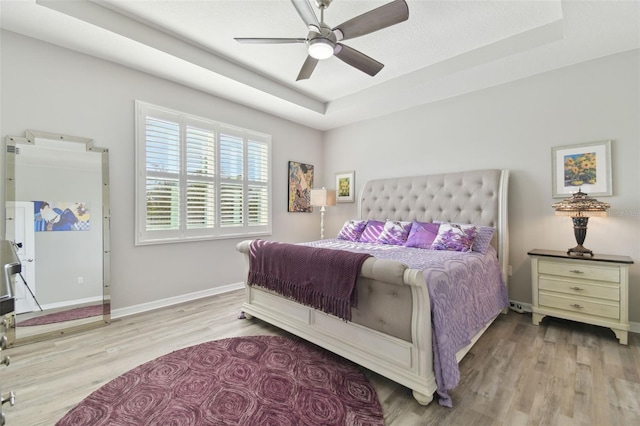 bedroom featuring ceiling fan, a raised ceiling, and light hardwood / wood-style floors