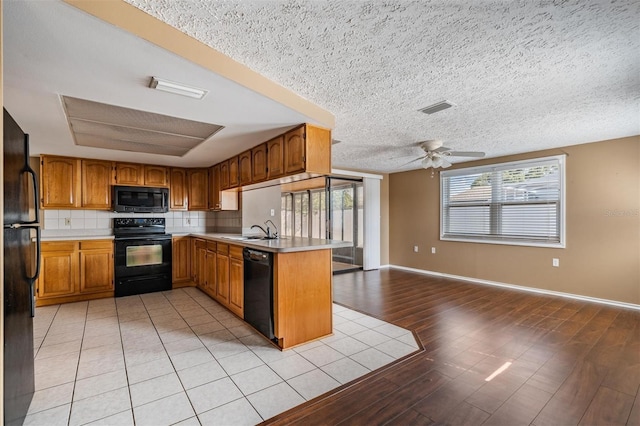 kitchen with sink, tasteful backsplash, black appliances, kitchen peninsula, and light wood-type flooring