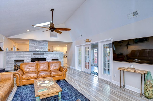 living room with ceiling fan, high vaulted ceiling, wood-type flooring, a stone fireplace, and french doors