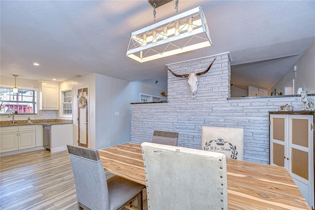 dining area with vaulted ceiling, sink, a textured ceiling, and light wood-type flooring