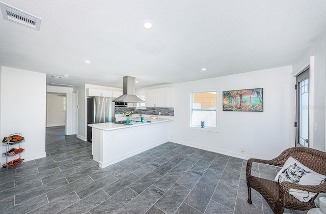 kitchen with visible vents, decorative backsplash, white cabinets, island range hood, and a peninsula