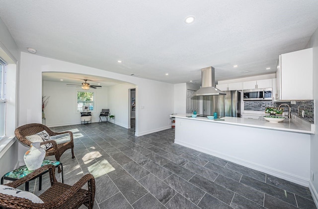 kitchen featuring arched walkways, white cabinets, appliances with stainless steel finishes, tasteful backsplash, and island exhaust hood