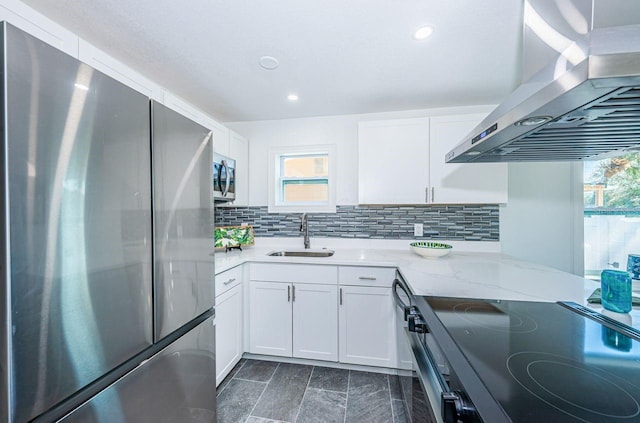 kitchen featuring wall chimney exhaust hood, appliances with stainless steel finishes, a sink, and decorative backsplash