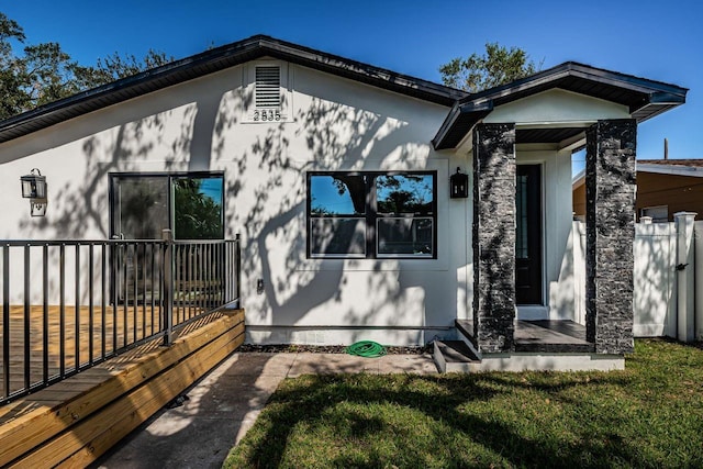 view of side of home with a lawn, fence, and stucco siding