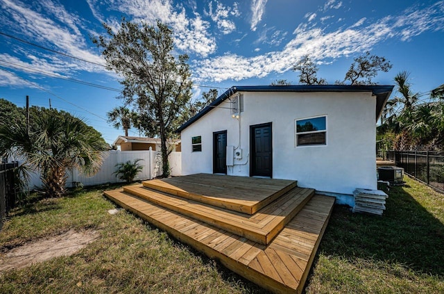 rear view of property featuring a fenced backyard, a wooden deck, a lawn, and stucco siding