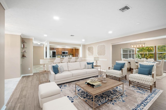 living room with crown molding, an inviting chandelier, and light wood-type flooring