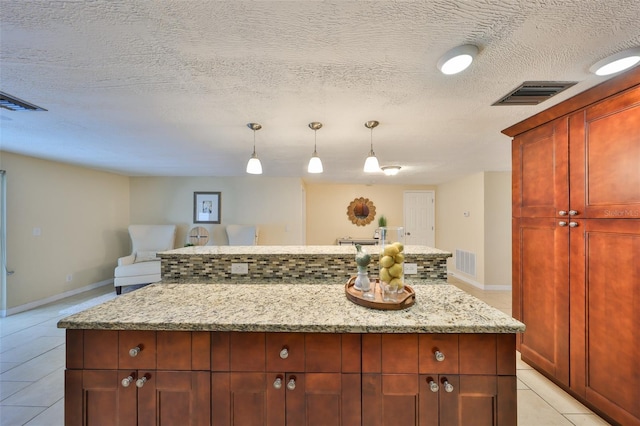 kitchen with hanging light fixtures, light stone countertops, light tile patterned floors, and a textured ceiling