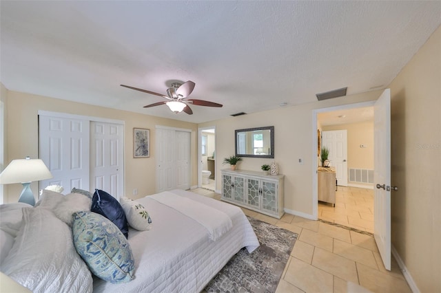 bedroom featuring light tile patterned floors, ensuite bath, ceiling fan, a textured ceiling, and two closets