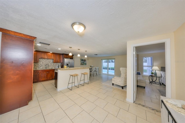 kitchen with pendant lighting, a breakfast bar area, stainless steel refrigerator with ice dispenser, tasteful backsplash, and light tile patterned flooring