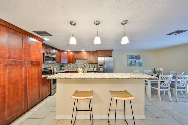 kitchen featuring light tile patterned flooring, a breakfast bar, decorative light fixtures, tasteful backsplash, and stainless steel appliances