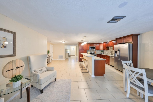 kitchen with a breakfast bar, pendant lighting, backsplash, stainless steel appliances, and a textured ceiling