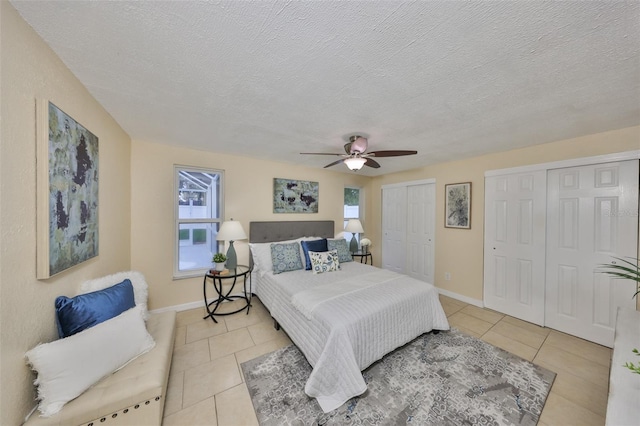 bedroom featuring ceiling fan, light tile patterned floors, a textured ceiling, and two closets