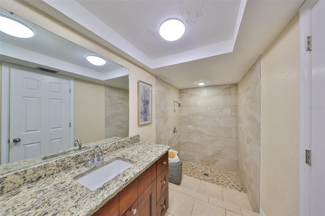 bathroom featuring a tile shower, vanity, tile patterned flooring, and a textured ceiling