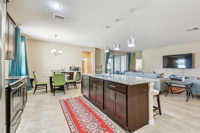 kitchen featuring a kitchen bar, hanging light fixtures, a center island with sink, stainless steel appliances, and light stone countertops