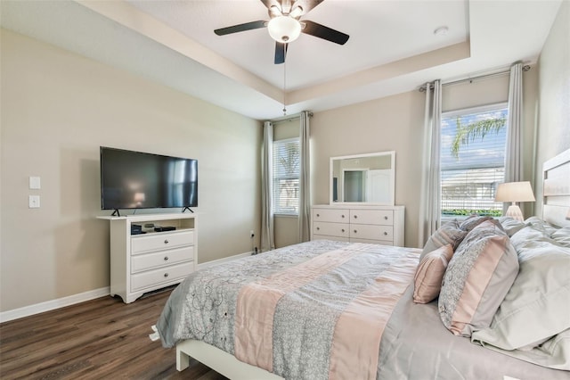 bedroom featuring a tray ceiling, baseboards, dark wood-type flooring, and a ceiling fan