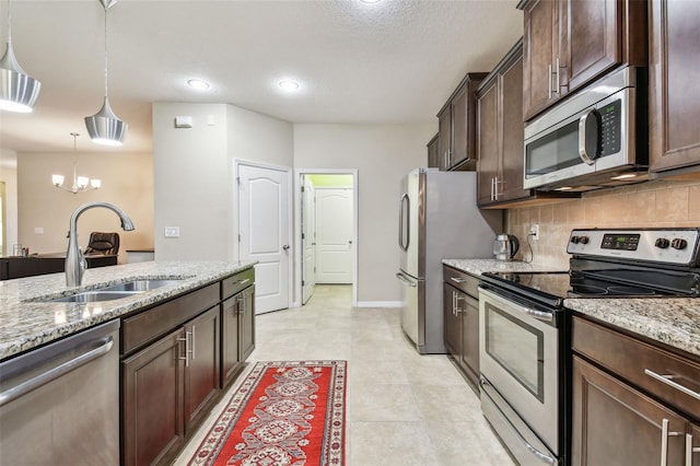 kitchen featuring light stone countertops, a sink, stainless steel appliances, dark brown cabinetry, and backsplash