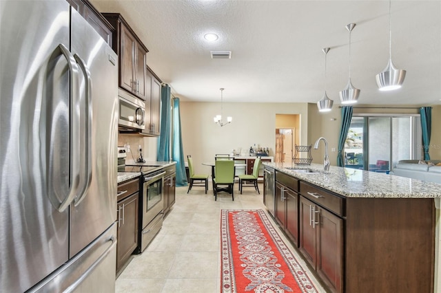 kitchen featuring pendant lighting, sink, appliances with stainless steel finishes, dark brown cabinets, and an island with sink