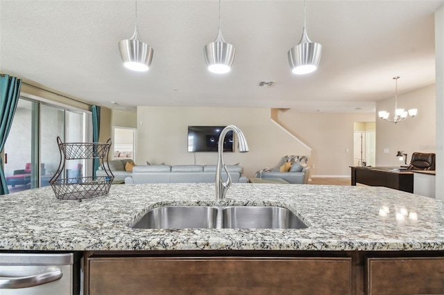 kitchen with light stone counters, sink, hanging light fixtures, and a center island with sink