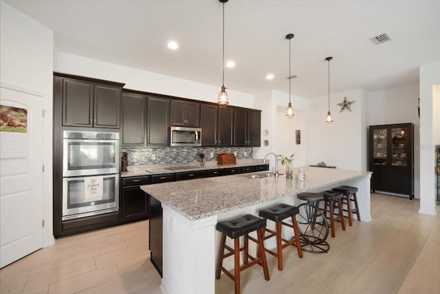 kitchen featuring decorative light fixtures, a breakfast bar area, decorative backsplash, stainless steel appliances, and a center island with sink